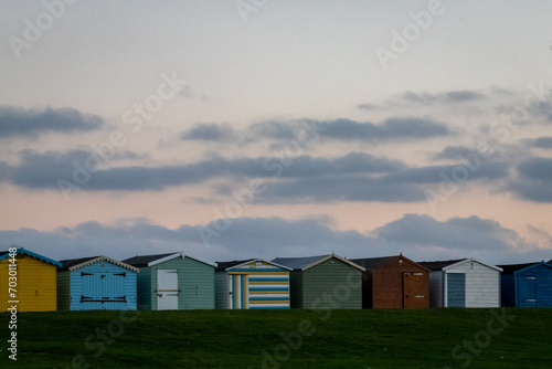 Sunset over beach huts along the Essex coast, Image shows a range of different colours and styles of beach huts with a slightly cloudy sky showing various colours