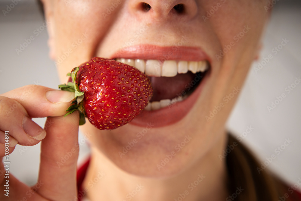 Young woman enjoying biting a strawberry on a light background, closeup Young woman enjoying biting a strawberry on a light background, closeup