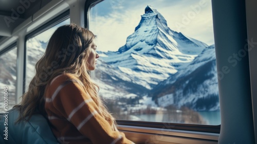 A girl sits on a train and looks out the window at a snowy mountain