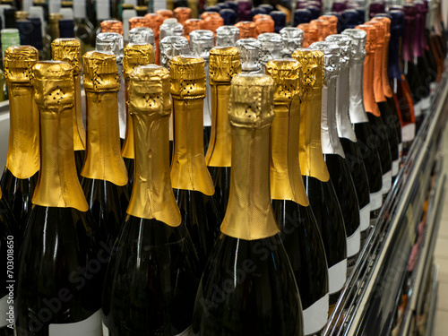 The batch of sparkling wine or Champagne bottles stand in a row on the wine store shelf. Selective focus.