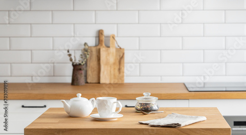 Wooden oak table with a cup of tea and a kettle  in front of the kitchen with a white brick background. photo