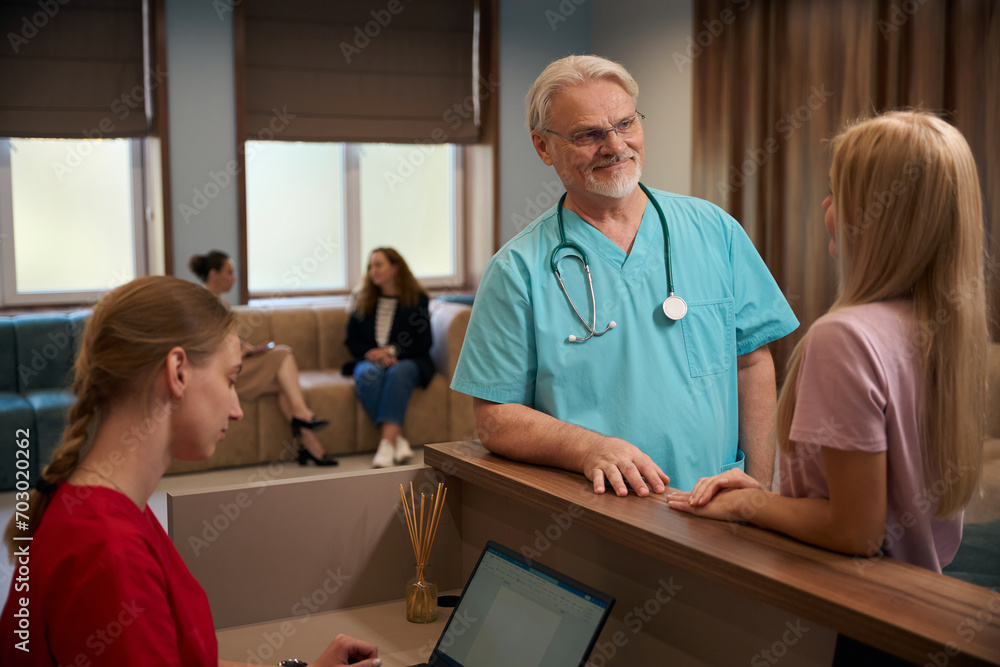 Fototapeta premium Friendly physician having conversation with female patient in clinic lobby