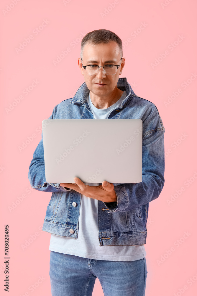 Mature male programmer with laptop on pink background Mature male programmer with laptop on pink background