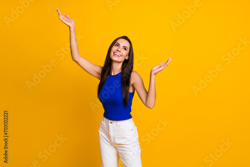 Photo of carefree cheerful woman wear blue top rising hands arms looking empty space isolated yellow color background