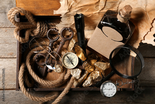 Box with travel equipment, golden nuggets and bottle of rum on brown wooden background photo