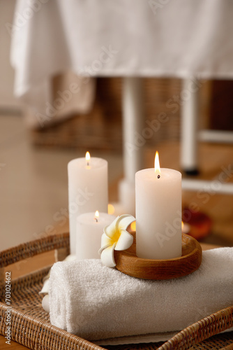 Burning candles with flowers and towel on table in spa salon  closeup