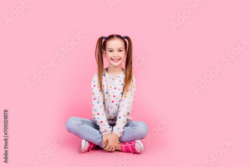 Full length photo of positive cheerful girl wear stylish sweatshirt jeans pants sitting on floor isolated on pink color background photo