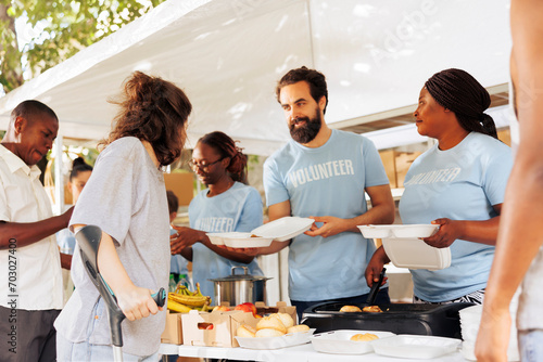 Multiethnic group of volunteers provides aid, handing out free food to disadvantaged communities. They support homeless, sick, and those in poverty. Charitable act of compassion and relief. photo