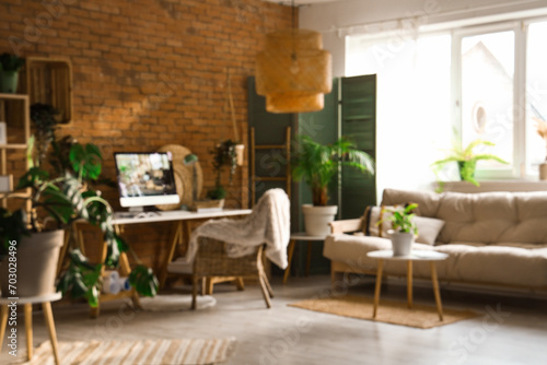 Blurred view of office with workplace, green plants and sofa © Pixel-Shot