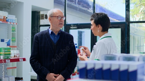Фотография Older client in need of prescription affliction healing drug informations in apothecary, asking experienced pharmacist