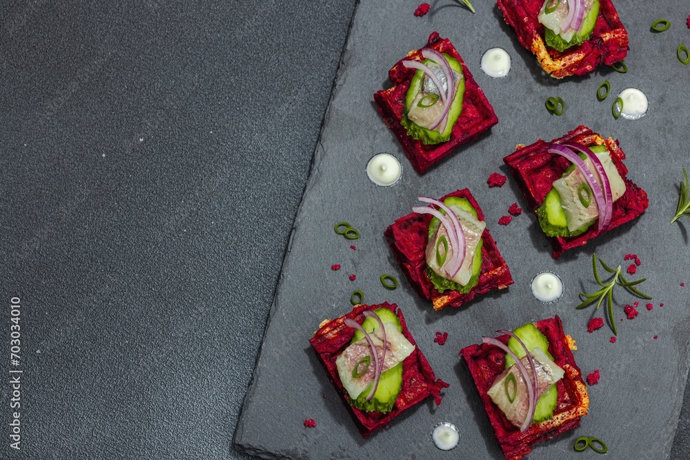 A delicious festive appetizer with herring on pieces of beet waffles with spices and sauce