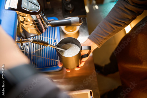 Coffee maker or bartender whisking milk for latte in steel jug in coffee house