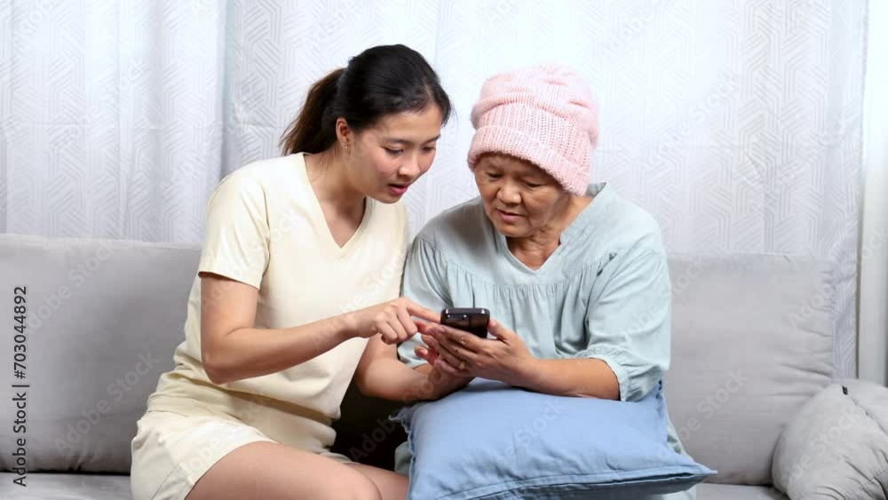 Asian caregiver nurse female taking care of cancer chemotherapy elderly senior woman at home, young daughter and sickness retired mother happy learning mobile phone application free time in holiday Asian caregiver nurse female taking care of cancer chemotherapy elderly senior woman at home, young daughter and sickness retired mother happy learning mobile phone application free time in holiday