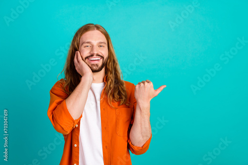 Photo of optimistic young hippie guy in orange shirt point thumb empty space twitter elon musk post isolated on blue color background photo