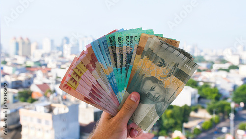 Man's Hand holding rupiah money against the backdrop of the capital of Indonesia. photo