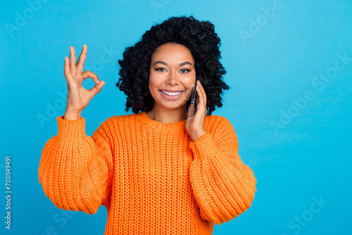 Photo portrait of young woman talk phone show okey symbol dressed stylish knitted orange clothes isolated on blue color background photo