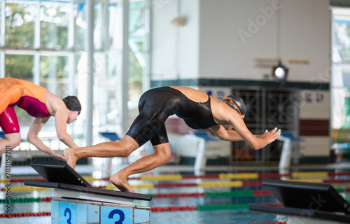 Two professional female swimmers taking track start position on the platform gracefully jumping and diving in a swimming pool. Sport competition concept. photo