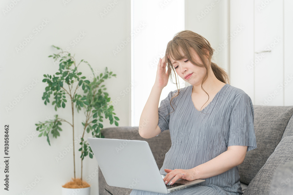 家のソファでパソコンを使って仕事する妊婦の女性・マタニティ・プレママ
