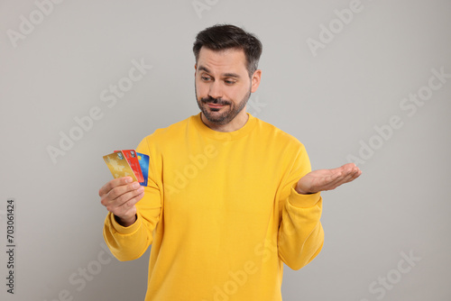 Confused man with credit cards on grey background. Debt problem