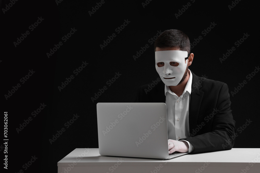 Man in mask and gloves working with laptop against black background. Space for text