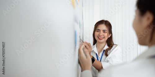 businesswoman writing strategy idea on sticky notes on whiteboard with colleague