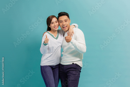 Happy young couple showing thumbs up and looking at camera isolated over blue background
