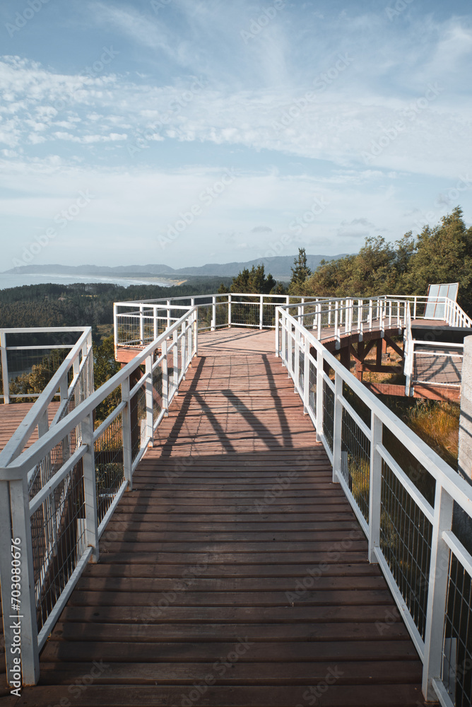 wooden bridge over the sea, viewpoint of the coastline, with a lot of trees in a mountain on a summer day