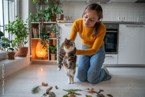 Tender caring pet owner showing to lazy uninterested cat natural objects, twigs brought from park, encouraging energy, interest, activity. Idle cat dreaming of lying, sleeping, resting, doing nothing photo