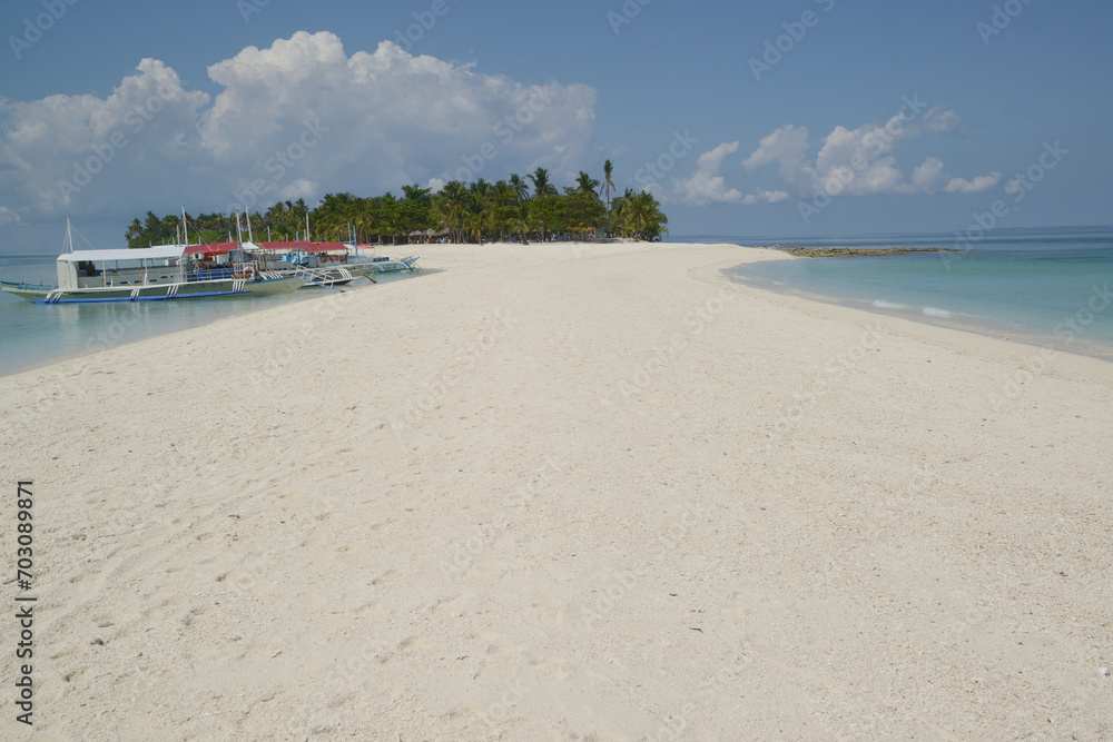 Beautiful white sand beach with palm trees on a hot, clear day and local traditional Filipino boats or Outrigger boats anchored.