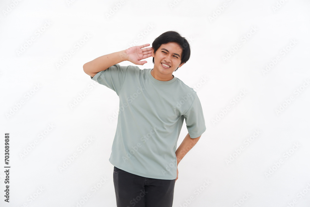 A young Asian man, an employee in a tshirt, is seen enthusiastically listening with his hand to his ear against a white background. A young Asian man, an employee in a tshirt, is seen enthusiastically listening with his hand to his ear against a white background.