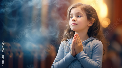 A young girl with closed eyes and clasped hands prays devoutly in a church, bathed in ethereal sunlight. photo