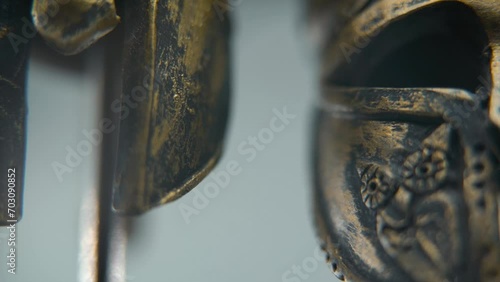 A close-up macro shot of a Spartan design, two different ancient warrior metal bronze helmets, textured shapes, studio lighting, Full HD cinematic video, hyper Slow Motion 120 fps, tilt up photo