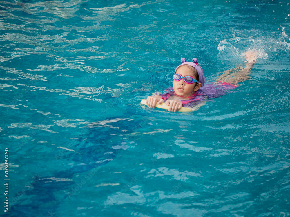 Asian child or kid girl wearing swimming suit to learning on swimming pool , learn and training swim on kick board