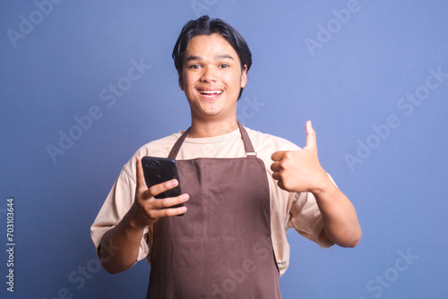 Cheerful young barista waiter male showing thumb up while holding smartphone © Queenmoonlite Studio