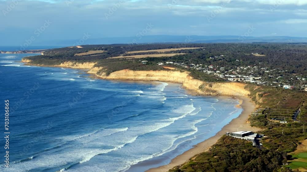 Coastal cliffs tower over a sweeping sandy beach, Waves gently breaking along the shoreline with a quaint town in the distance Coastal cliffs tower over a sweeping sandy beach, Waves gently breaking along the shoreline with a quaint town in the distance