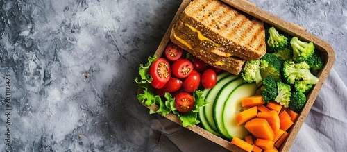 Top view of a nutritious lunch box with sandwich, vegetables, on a stone table. photo
