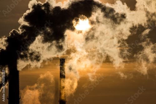 Silhouette of heavily smoking tall chimneys against the backdrop of the bright sun