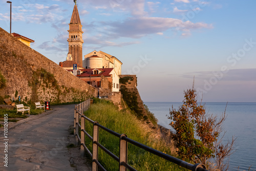 Scenic walking path between Fiesa and coastal town of Piran, Slovenian Istria, Slovenia, Europe. Scenic sunrise view of St George Parish Church. Shimmering waters of Adriatic Mediterranean Sea