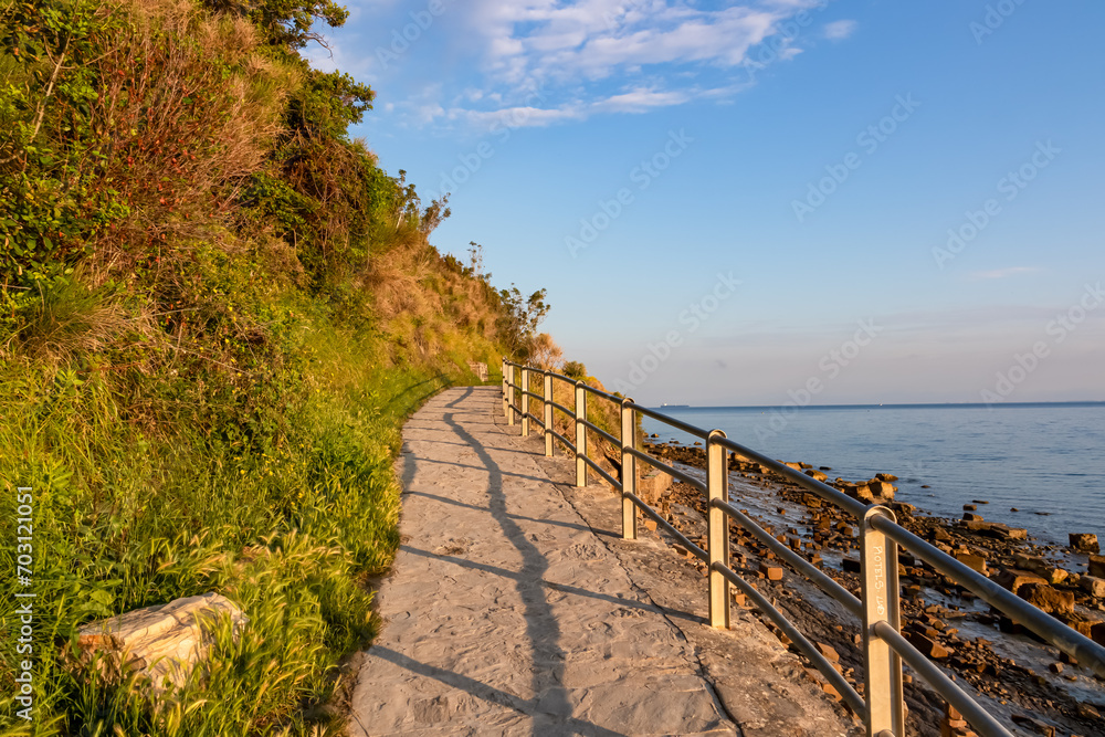 Fototapeta premium Scenic walking path between Fiesa and charming coastal town of Piran in Slovenian Istria, Slovenia, Europe. Rugged rocky cliffs gracefully perched above shimmering waters of the Adriatic Sea. Seascape