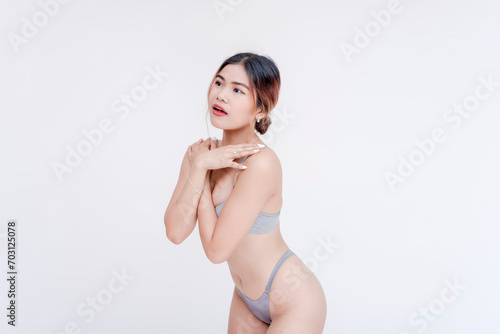 фотографія An embarrassed and flustered woman covers her breasts covered only in a gray bra after being undressed and exposed in her underwear