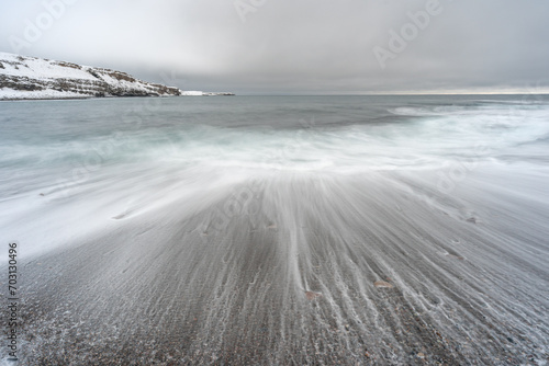 Tranquil ocean waves crash against sandy shore under cloudy sky. Ekkerøya, Northern Norway photo