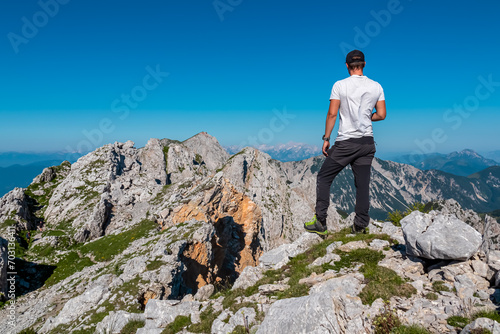 Hiker man with scenic view of majestic mountain peak Hochstuhl (Stol) in untamed Karawanks, border Slovenia Austria. Looking from Vertatscha peak. Wanderlust in wilderness of Slovenian Alps in summer