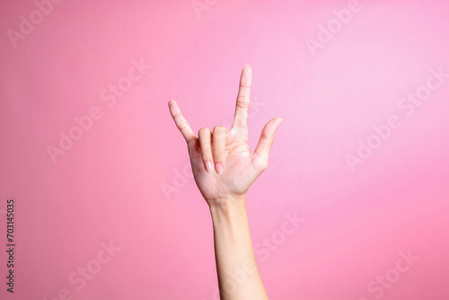 Hand showing rock sign with fingers gesture against pink background, human hand gesture photo