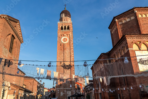 Sunrise view of bell tower of Cathedral Santa Maria Assunta in charming town of Chioggia, Venetian Lagoon, Veneto, Italy. Decoration Sagra del Pesce in foreground. First sun beams on landmark photo