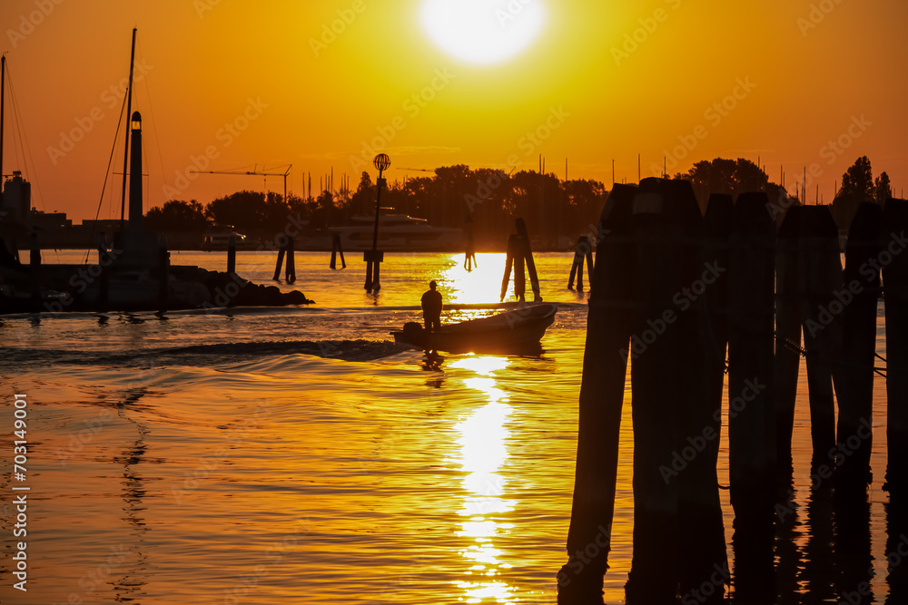 Silhouette of bricolas and boats in picturesque port of charming town of Chioggia at sunrise, Venetian Lagoon, Veneto, Italy. Warm colors and tranquil atmosphere in summer. Magical bay in Adriatic sea