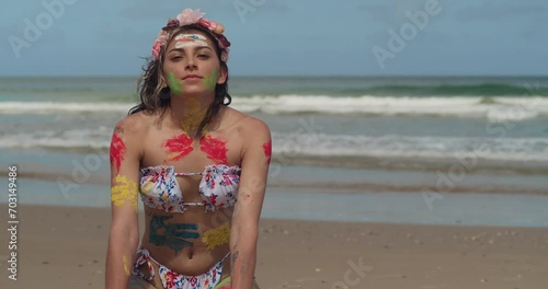 A youthful girl, clad in a bikini, adorned with body paint, graced a sunlit Tropical beach in the Caribbean. photo