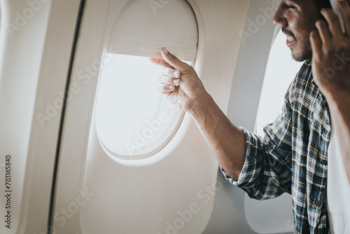 Asian man on an airplane looking out the window with headphones on, possibly enjoying music or an audiobook during his flight. photo