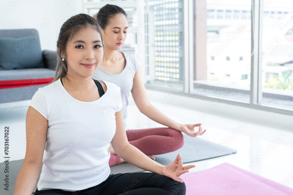 Two Young beautiful asian sport women sitting on the yoga mat practicing meditation. Fitness or exercise at home. Beautiful females relaxing after workout. Two Young beautiful asian sport women sitting on the yoga mat practicing meditation. Fitness or exercise at home. Beautiful females relaxing after workout.