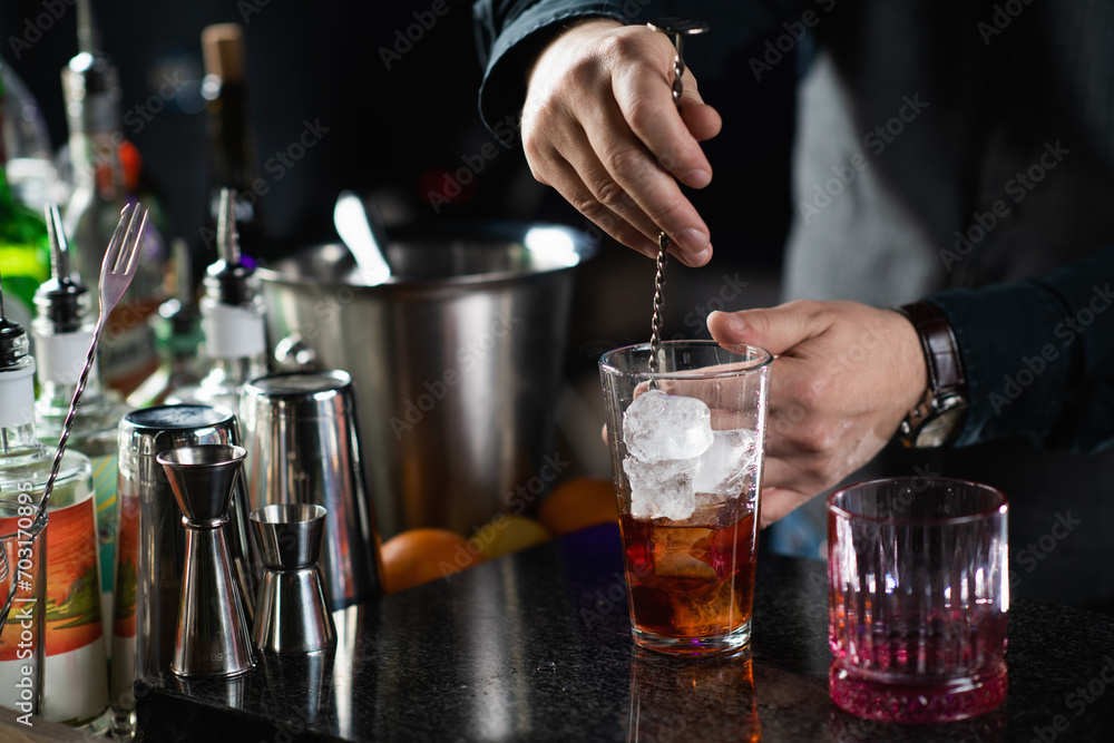 Bartender mixing Negroni cocktail with long stirring metal spoon