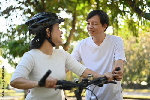 Cheerful middle aged couple riding bicycles in public park together. Healthy lifestyle concept.